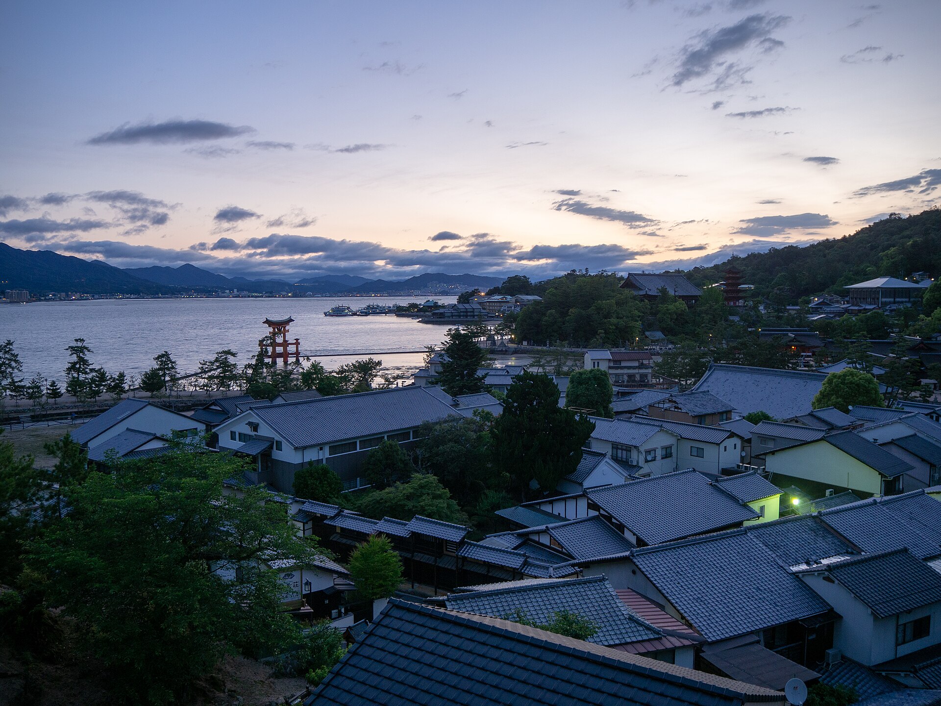 Amanecer sobre Miyajima desde un ryokan: tejados del pueblo, gran torii y pagoda