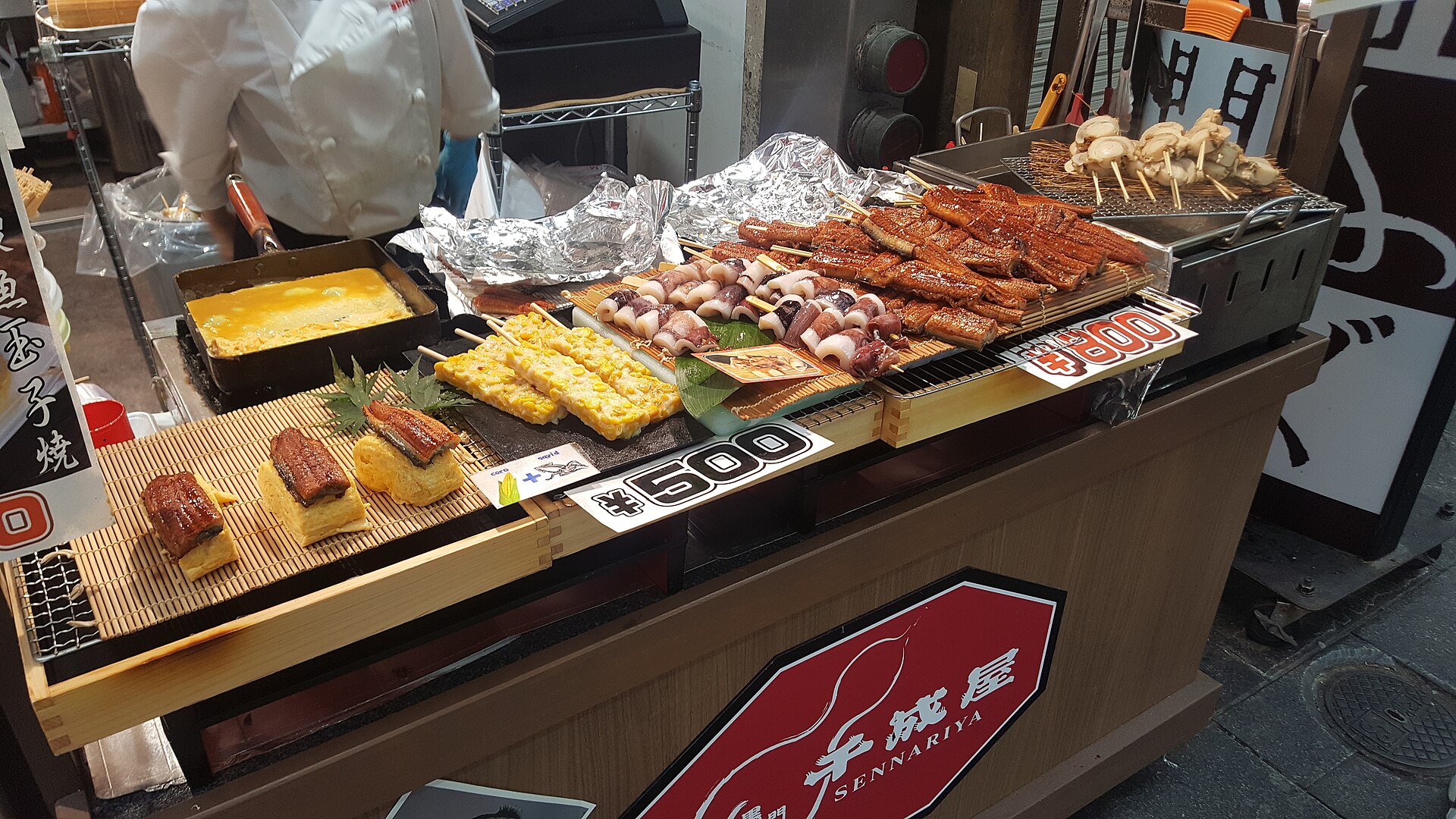 Brochetas de anguila y calamar a la parrilla y tortilla japonesa en un puesto del mercado de Kuromon